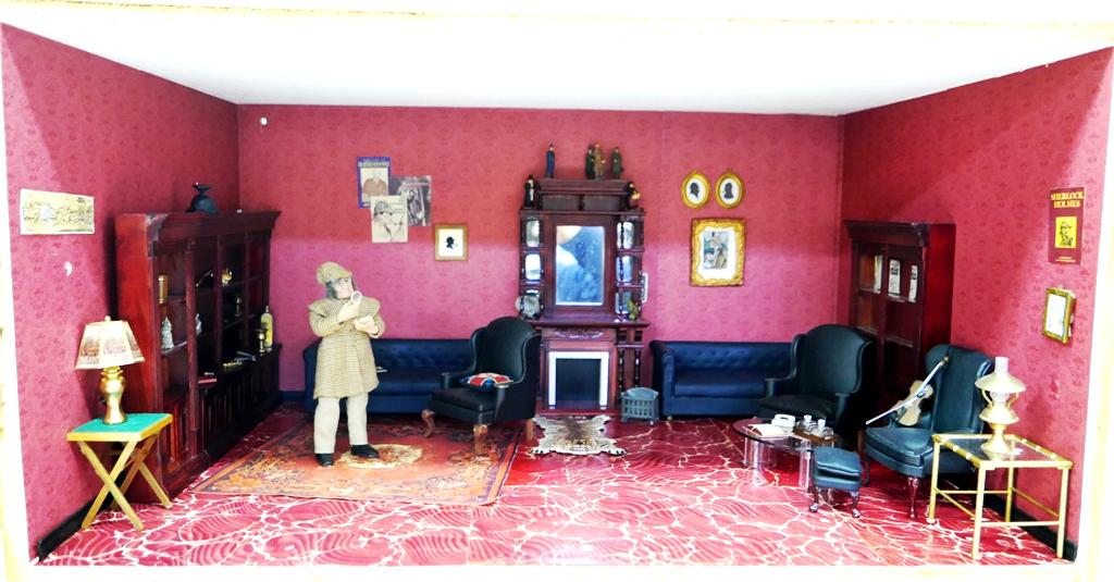 Sherlock Holmes Living Room Krupick, Box Dollhouse: Plywood room box with hinged front cover, interior has painted ceiling, paper covered walls and floor, wood fireplace with mirrors has painted pewter figurines, pair of tufted sofa, three armchairs an