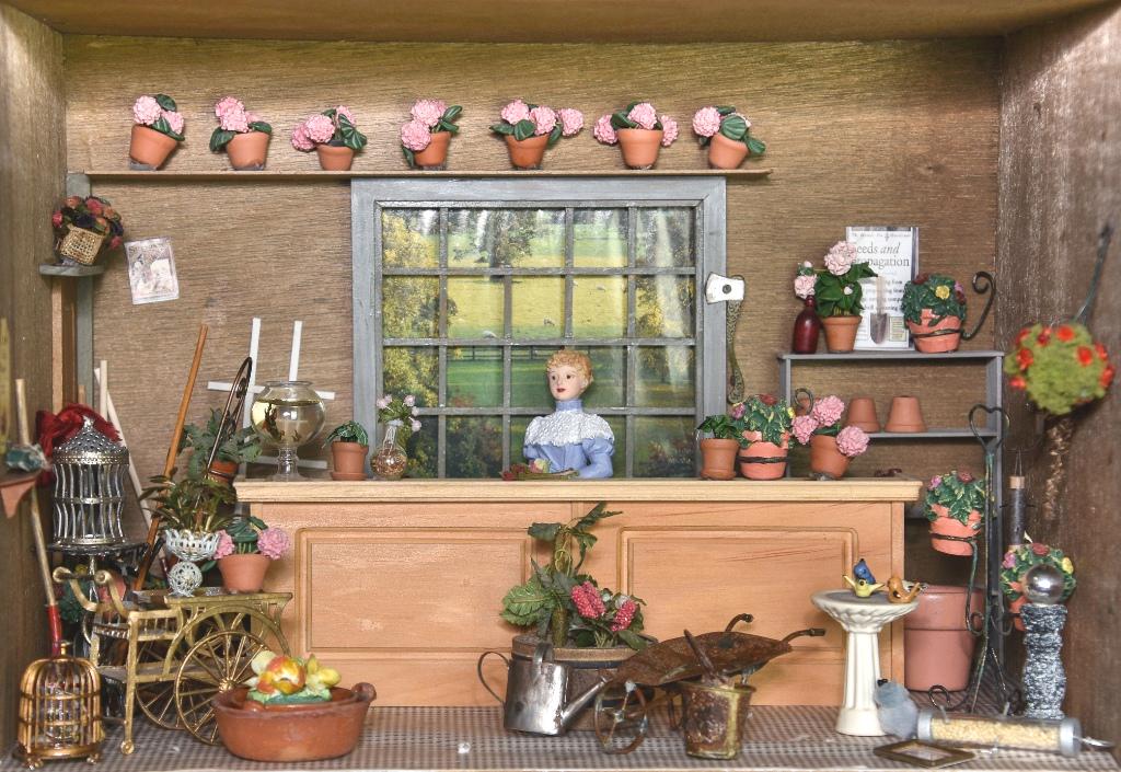 Garden Shop Room Box Dollhouse: Small wood room box 16"W, 10"D, 11"H, filled with a wood counter, resin doll, vintage soft metal birdcages and stand, shelving unit with flowers and pots, gardening supplies etc.