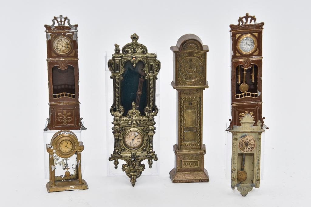 Antique Dollhouse Clock Miniatures: Very ornate cast metal wall clock 6.25"H moves hands and pendulum when wheel on side is turned, two soft metal tall case clocks 5"H, soft metal wall clock missing finial 3.5"H and mantel clock 2.5"H,