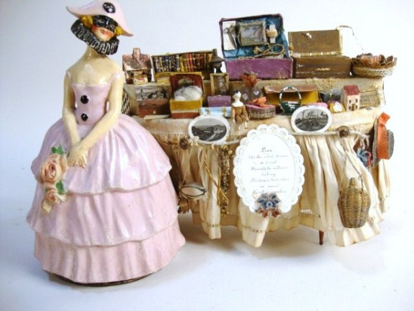 Unusual Peddler-type Table and Candy Container: An interesting display of sewing boxes, vanity cases, jewelry boxes, dolls, all sorts of ephemera assembled on a table 9" W with one leg loose but present, perhaps created for a peddler doll, offered 