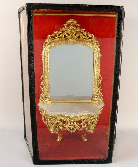French Mirrored Console: Very ornate wall console 21" H with mirrored back, faux marble top and ornately modeled gilt metal frame, encased in a glass display cabinet that shows wear.