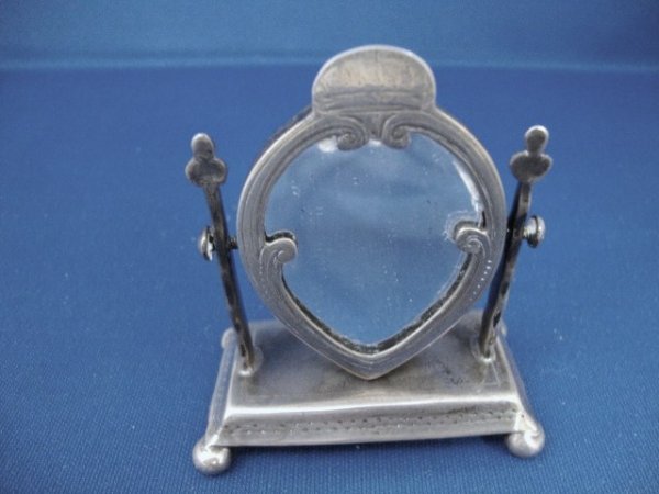 Standing Vanity Mirror from Lady Astor's Doll Hous: Standing mirror on rectangular platform with four ball feet, the mirror supported by two posts and pivoting at its mid-point, the frame of a broad dart-form engraved with scrolling along the side and 
