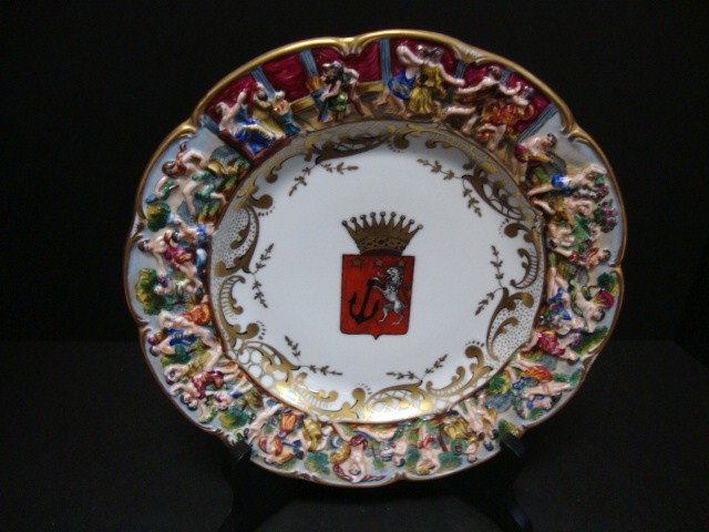 Capodimonte Coat of Arms Plate: Hand painted coat of arms plate with central crest of standing lion, holding anchor surmounted by 3 gold stars, all within a red shield topped by a gold crown scalloped gold rim, 10" diameter rim deco