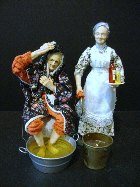 Dawn Adams Older Couple: A seated man soaking his feet and nursing an illness, and his wife 5.25" H, bringing medicine and more hot water, both by artisan Dawn Adams and featuring wonderful character faces.