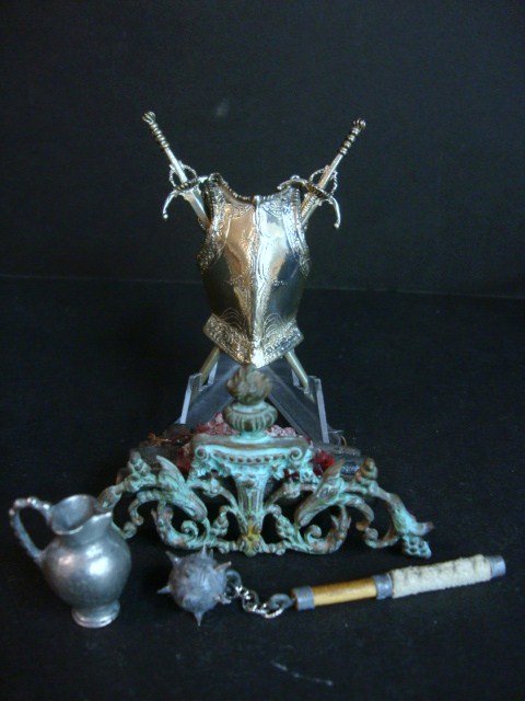 Brooke Tucker Firegrate: An electrified glowing pile of logs resting in an elaborate cast metal firegrate with verdigris finish by Brooke Tucker, a brass Conquistadore breast plate with crossed swords 3"H, a Tudor era mace an