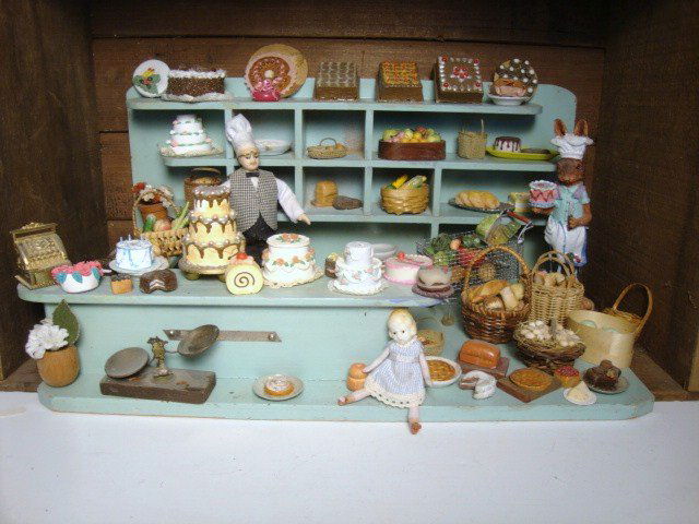 Bakery Roombox: A vintage German shop set inside an antique box crate and furnished with dozens of vintage and contemporary cakes, breads and pastries. A doll dressed as a baker, vintage bisque girl and a fantasy bun
