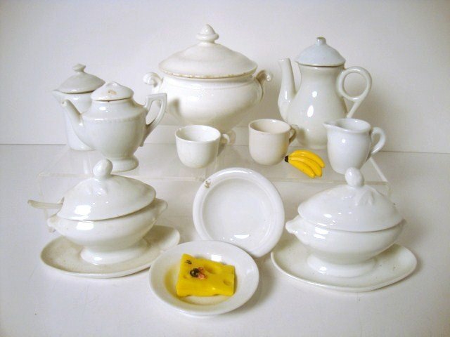 Doll's White Ironstone: An assortment of white glazed toy china including a round covered tureen 4" H and W, two smaller oval tureens, two teapots, a coffeepot, a pitcher, two cups and two shallow bowls, one with foodstuffs.