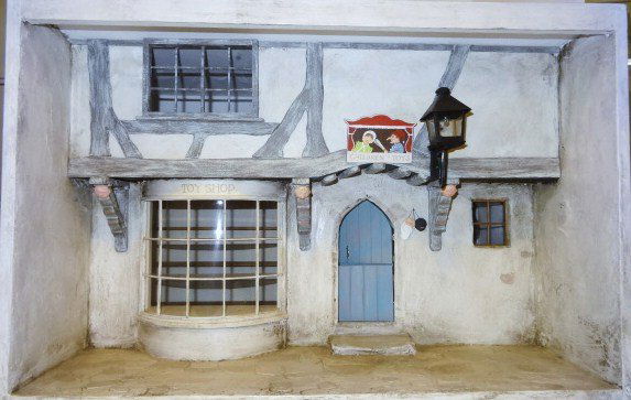 Robert Bernhard Toy Shop Roombox: Beautifully rendered storefront by Dolphin Originals that opens from the back for furnishing. The streetscape features a large bow window with individual panes, a pretty Gothic doorway, impressive car