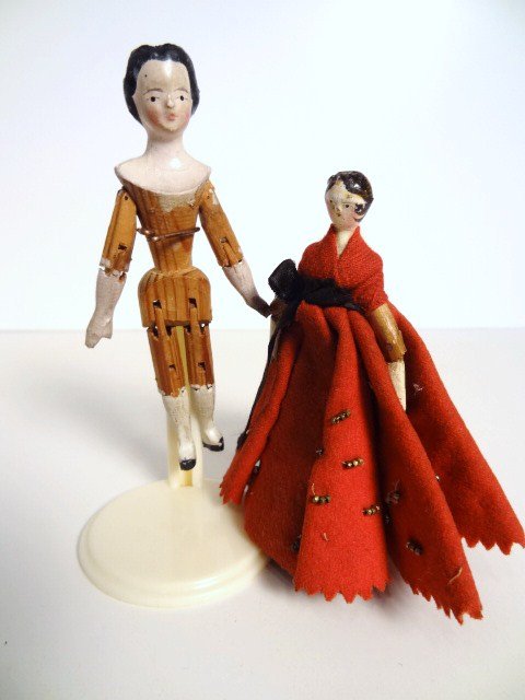 Miniature Peg Wooden Dolls: Two peg wooden dolls,the taller is 3.75" H with a fully jointed carved wooden body, painted lower arms and legs, she boasts a wistful expression and an unusual hairdo with bun in the back, tiny black
