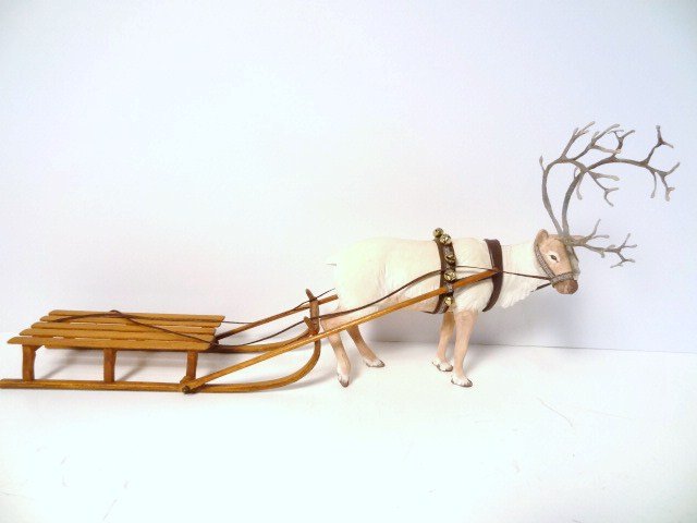 Artisan Reindeer and Sleigh: A Sylvia Mobley dashing reindeer 5.5" H, 6" L with a flat wooden sleigh. One antler appears to have been reglued in place.
