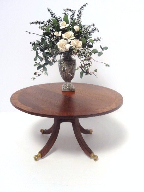 Escutcheon Table with Flowers: A mahogany breakfast table with banded edging (small glue edge showing) and brass casters 2.25" H, 4.25" diameter, with a flamboyant arrangement of white roses.