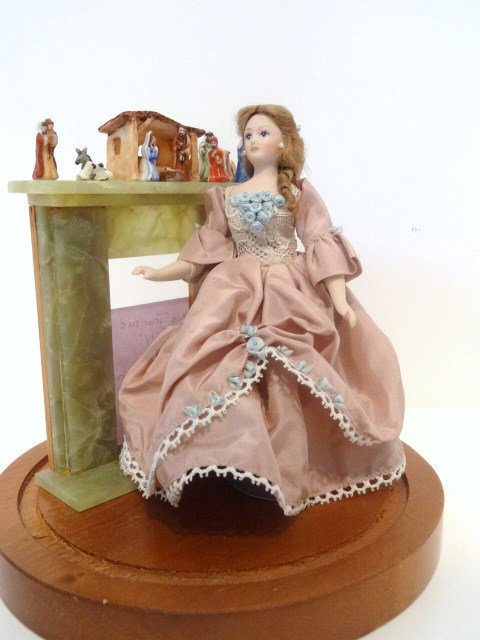 Artisan Christmas Dome: Several artists are represented in this small vignette under a dome including a Carol Boyd nicely coiffed and dressed lady doll standing before a marble fireplace by Braxton Payne, with a Nativity set