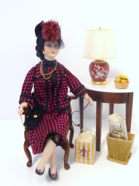 The Fashionable Lady: A smartly dressed lady in a skirted suit, her clothing fashioned for a seated position, in a vignette composed of an upholstered corner chair from Ray Lewis who also finished the corner table, an elec