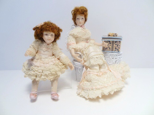 English Mother and Child: By Sue Atkinson, an Edwardian seated lady in an elaborate afternoon dress designed for a seated position, and her daughter, also intended to be seated. Wire wicker chair and table, and an empty gift b