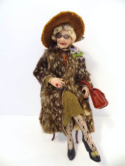 Marcia Backstrom Lady with Fur Coat: Seated and smiling elderly lady decked out in a real fur coat, net stockings, clutching a leather purse. One shoe buckle missing. 5" H.