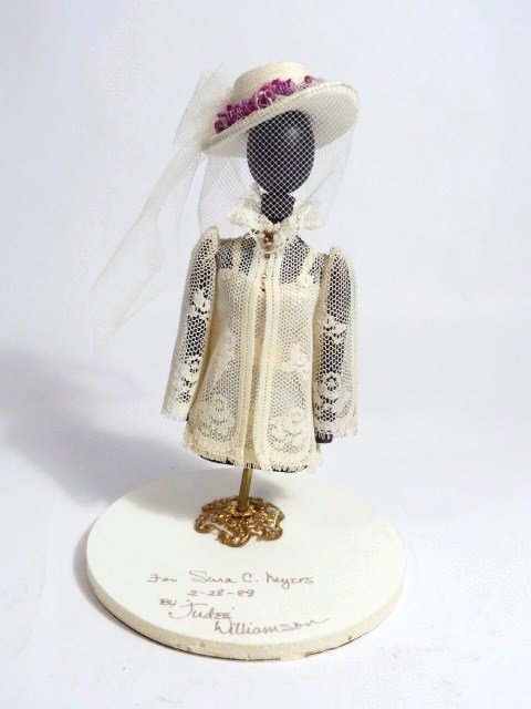 Judee' Williamson Mannequin: Charming dressed mannequin with gorgeous hat decorated with ribbon flowers 4.25" H, mounted on a foam core base that reads "For Sara C. Meyers 2-28-89 by Judee' Williamson". Base is loose.