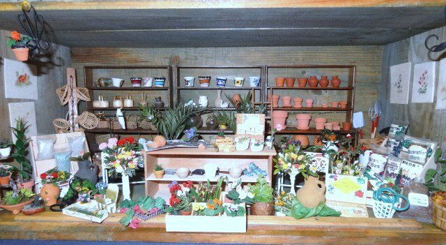 Potting Shed Roombox: Inside an antique crate 9.5" H, 23" W, 11" D, a setting of display shelves with potted flowers, seed packets, soil, tools, etc.