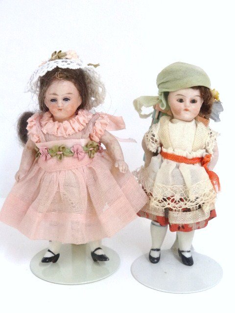 Two Bisque Girl Dolls: German all bisque girl doll, 3 1/2 in. w/blue glass eyes, original auburn mohair wig, original ivory & orange dress, doll carries a basket of flowers on her back like a backpack, painted black shoes w