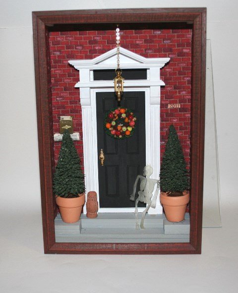 Front Entrance Shadow Box: Titled "Holiday Traditions 2011" and made by Carol Ann Frost, a shadow box featuring a formal house entrance flanked with potted evergreens and sporting a very handsome autumnal wreath. 12" H, 8" W, 3