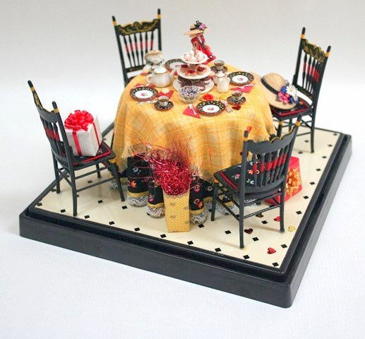 Mary Engelbreit Tea Party: Under a soft acrylic cover, a table for four decorated with items befitting a jolly celebration. Round table with four Chrysnbon chairs featuring a doll-size figure of Estelle, plates, cups and saucer