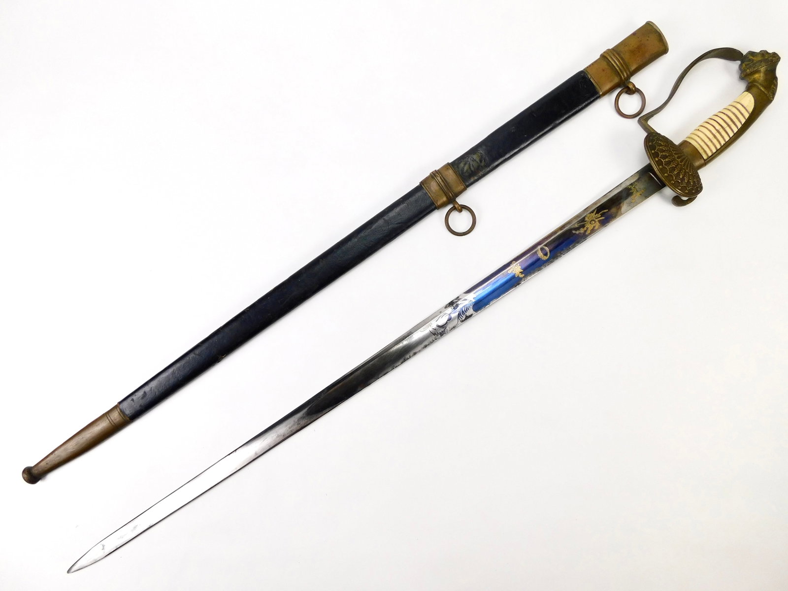Antique Early 19th Century German Lion Head Officer’s Sword Blued & Gilt Blade with Scabbard: In House Shipping. Antique German officer’s sword, attributed to the early 19th century, with scabbard. Features an ornate lion-head pommel, ribbed ox bone grip, decorative brass-tone guard and a bl