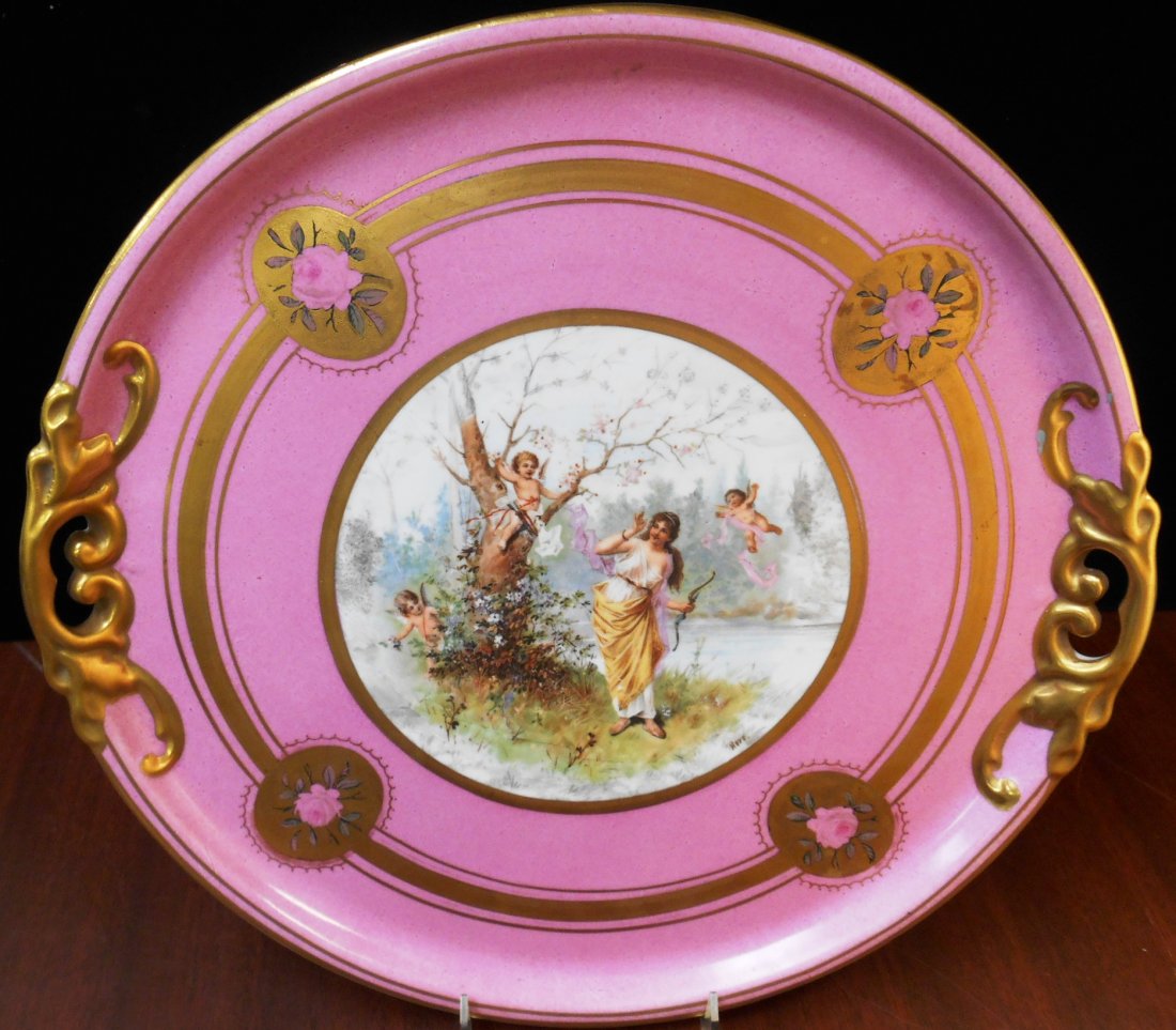 ROYAL VIENNA HAND PAINTED SIGNED PORCELAIN PLATTER: Incredible Scene of Cherubs surrounding a Beautiful Maiden holding A Bow in her right Hand. Pink with Gold Gilt Floral Background. The back has Royal Vienna Logo measures 14 1/2" Diameter. Artist sign
