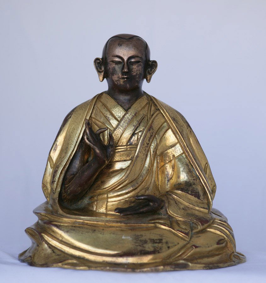 A striking Tibetan lama figure: Gilt bronze finish and superbly draped religious garments. Beautifully worked hands and face. 24.5cm high; 24cm wide.