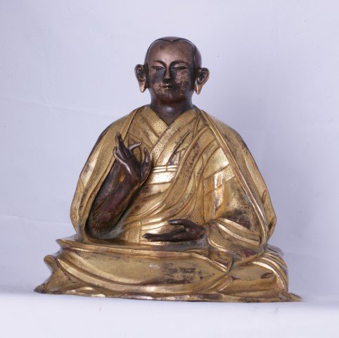 A Striking Tibetan Llama Figure: Gilt bronze finish and superbly draped religious garments. Beautifully worked hands and face. 24 x 24.5cm high.