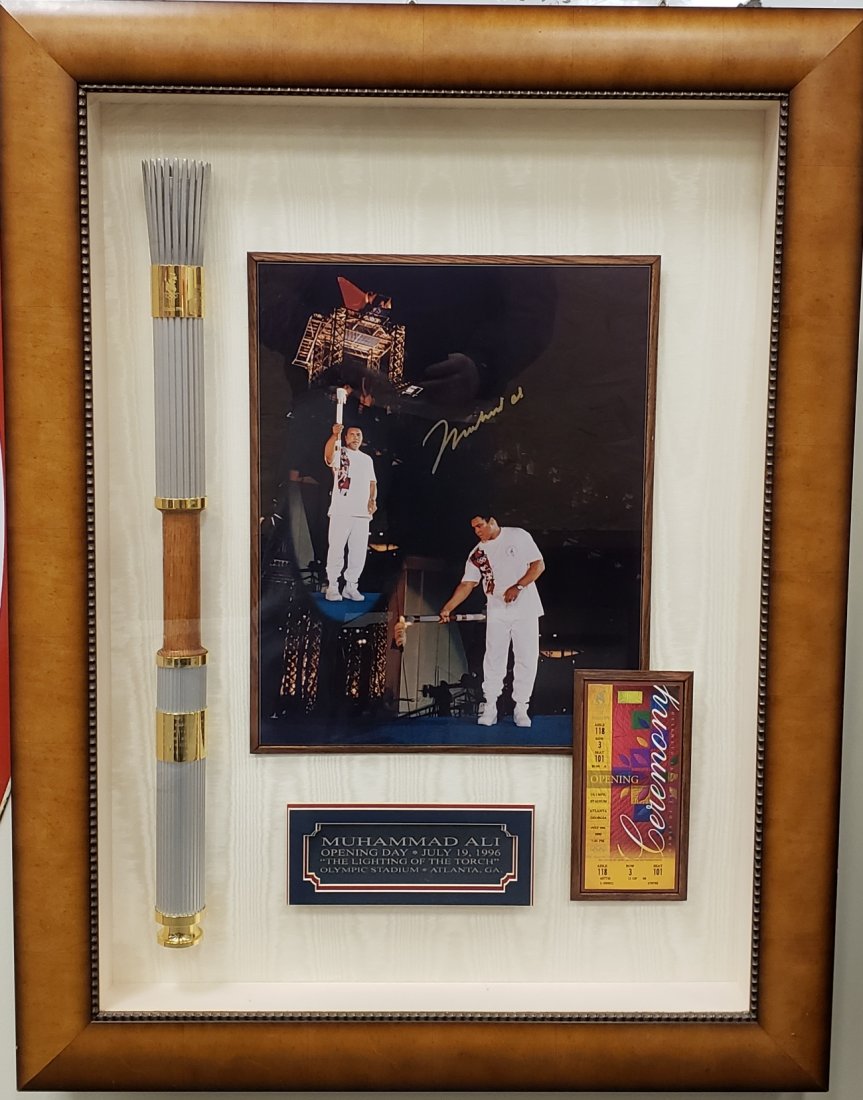 1996 Olympic Torch Signed Muhammad Ali Photo: 33" x 43.5" Beautifully framed shadow box of an original Atlanta Ga. 1996 opening day Olympic torch, an autographed photo of Muhammad Ali lighting the torch, and a ticket to the opening ceremony. The 