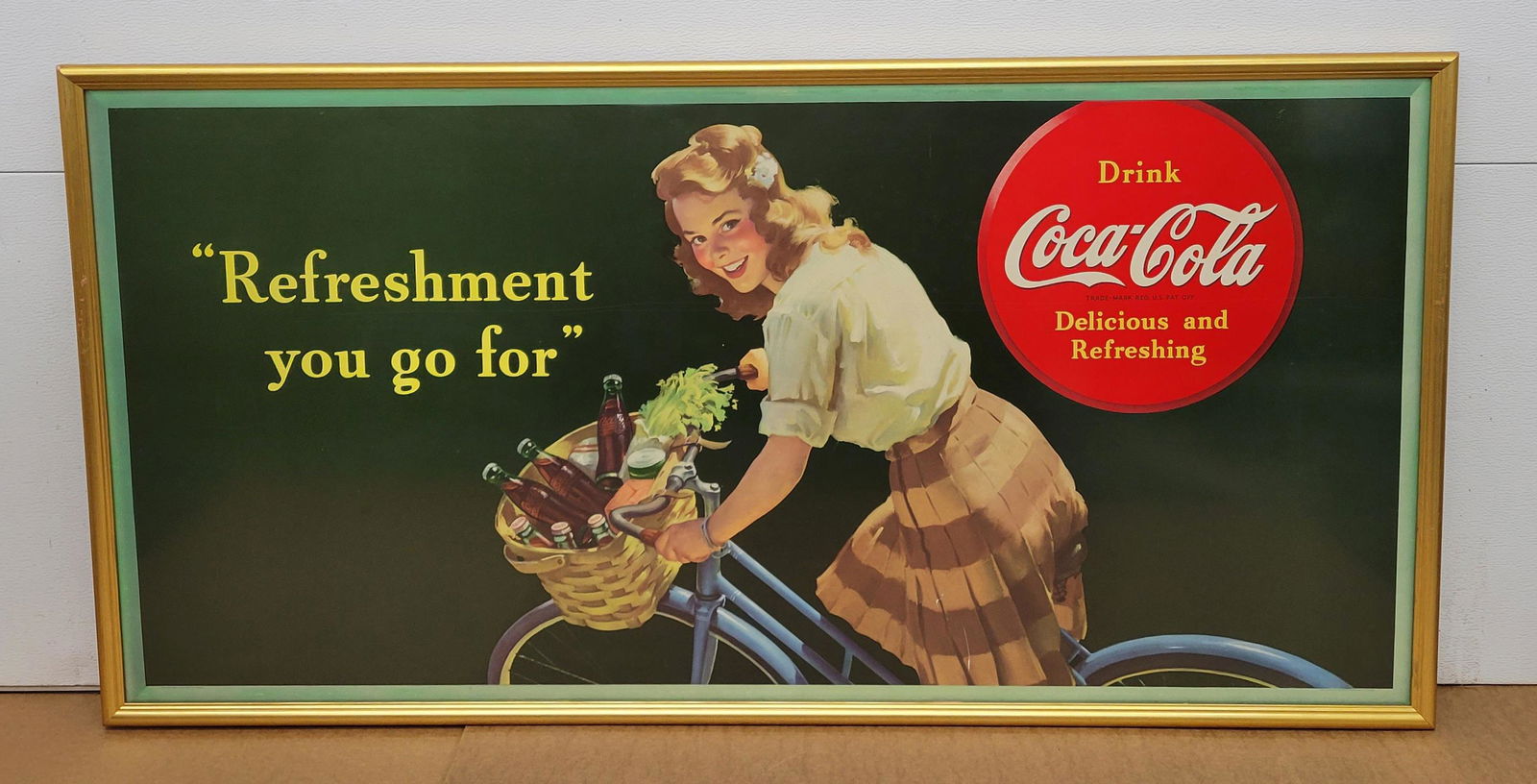 1944 Drink Coca Cola Delicious and Refreshing Cardboard In Frame: Coke. 58" x 27.25" - 1944 Coca Cola "Refreshment you go for" cardboard professionally framed under plexiglass with wire hanger and girl riding a bike scene. The colors are bright. There is a scratch o