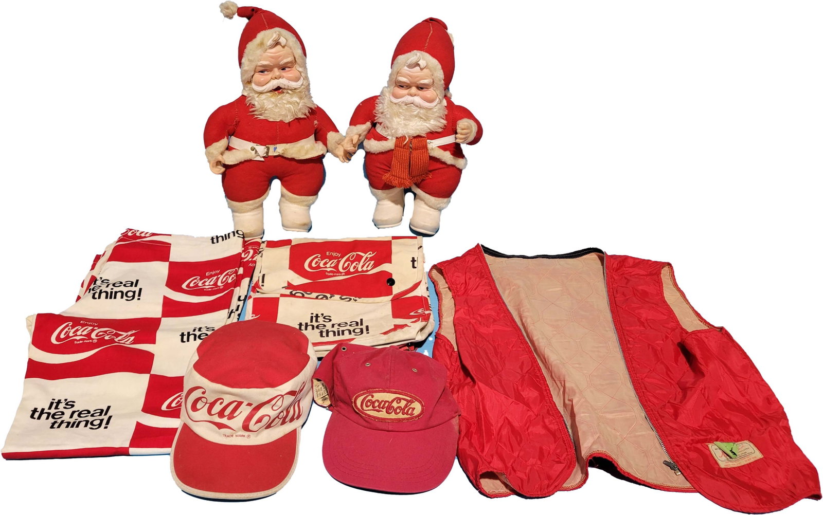Coca Cola Rushton Santas, pants, hats lot: 2 Rubber faced Rushton Coca Cola Santa Clauses with wear and minor tears in the stitching and belt, has a few stains. 2 Coca Cola hats in used condition, pair of Coca Cola Its The Real Thing pants and