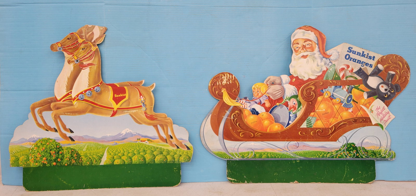Sunkist Oranges Double Sided Cardboard Signs With Santa, Sleigh and Reindeer: Lot of 2 DS cardboard signs includes a 24" x 18" sign with Santa and sleigh with bright colorful graphics exhibiting scuffs and scratches. There is a bend across Santa's face, a tear through the words