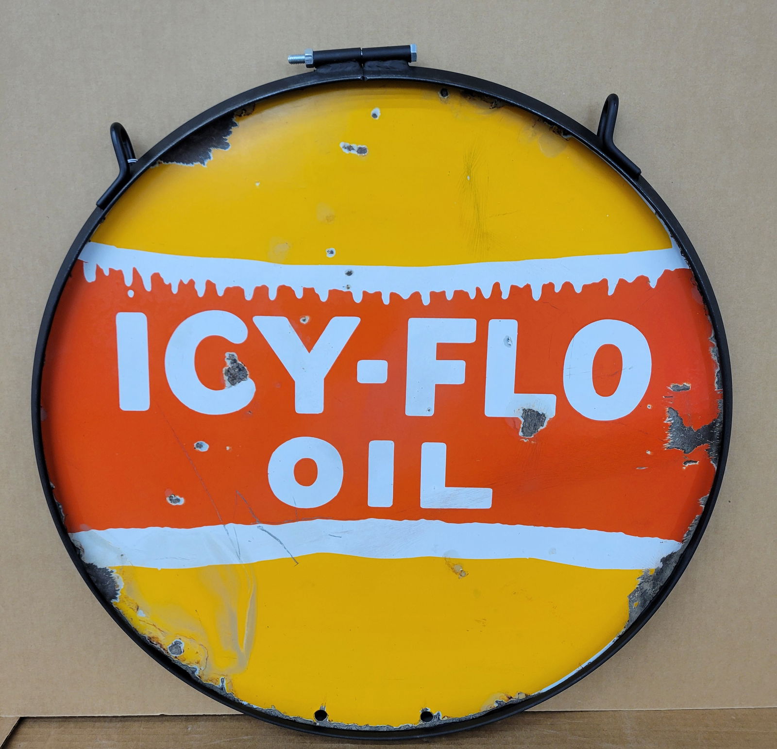 Icy-Flo Oil Double Sided Porcelain Sing In Ring: 24" DSP sign is mounted in a new ring. Both sides of the sign exhibit chips, cracks, and deep scratches with discoloration. The new ring is in excellent condition.