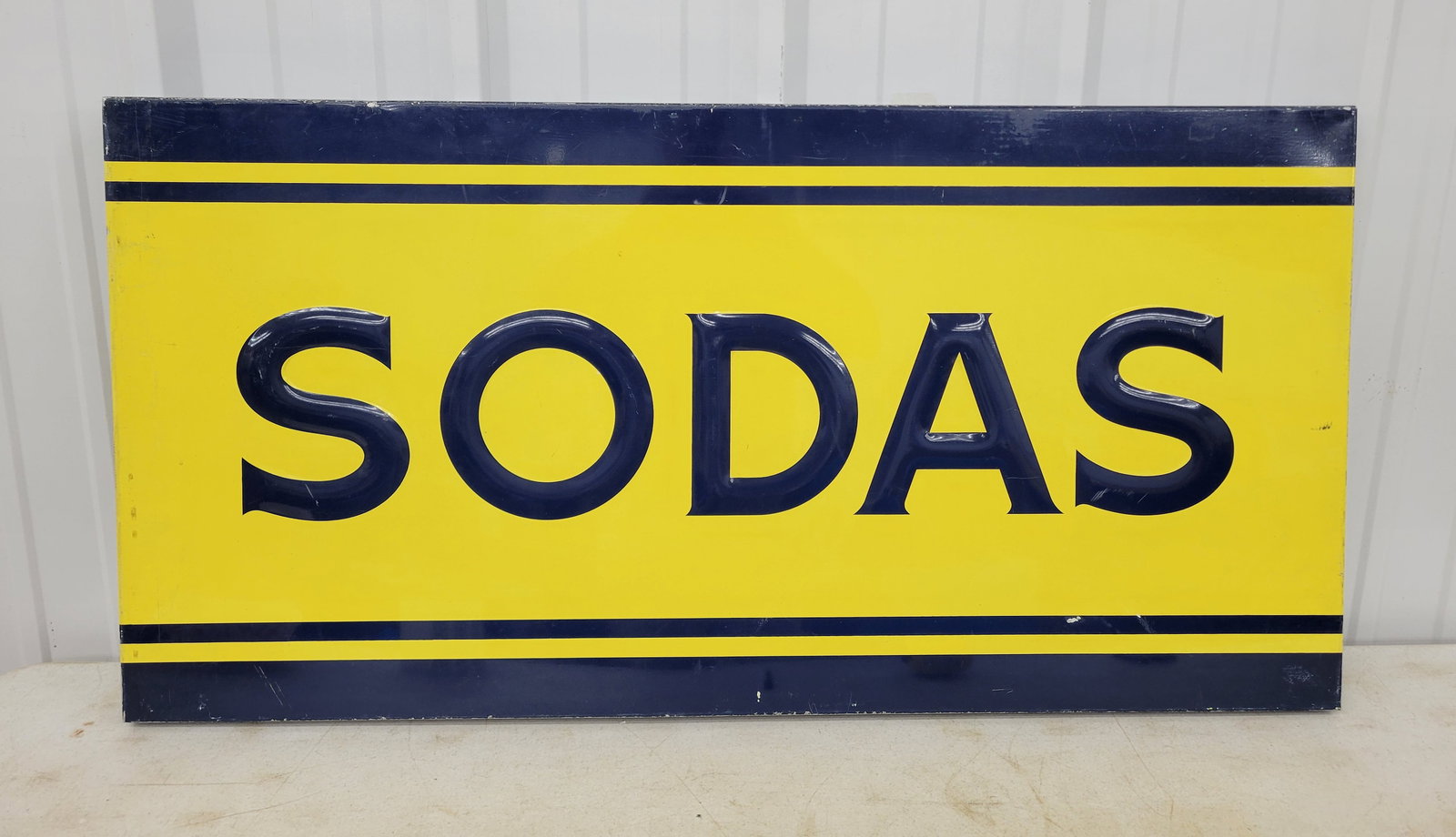 SODAS Embossed Single Sided Tin Sign: 48" x 24" has embossed lettering with good color and shine. There are light scuffs and scratches in the field and wear on the rolled edge perimeter.