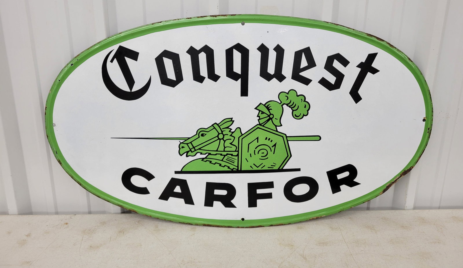 Conquest Carfor Single Sided Porcelain Sign: 43.5" x 24" self framed SSP sign showcases a knight on horseback, displaying vibrant colors and a glossy finish. The surface is mostly clean, except for a small flea bite chip located near the top and