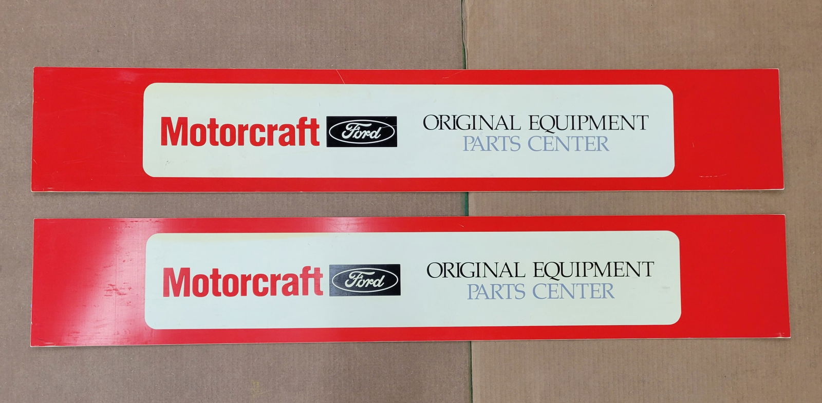 Ford Motorcraft Original Equipment Parts Center Signs: This lot includes two 48" x 8" plastic signs with light wear including minor scuffs. Toning is visible in the white areas of the signs.