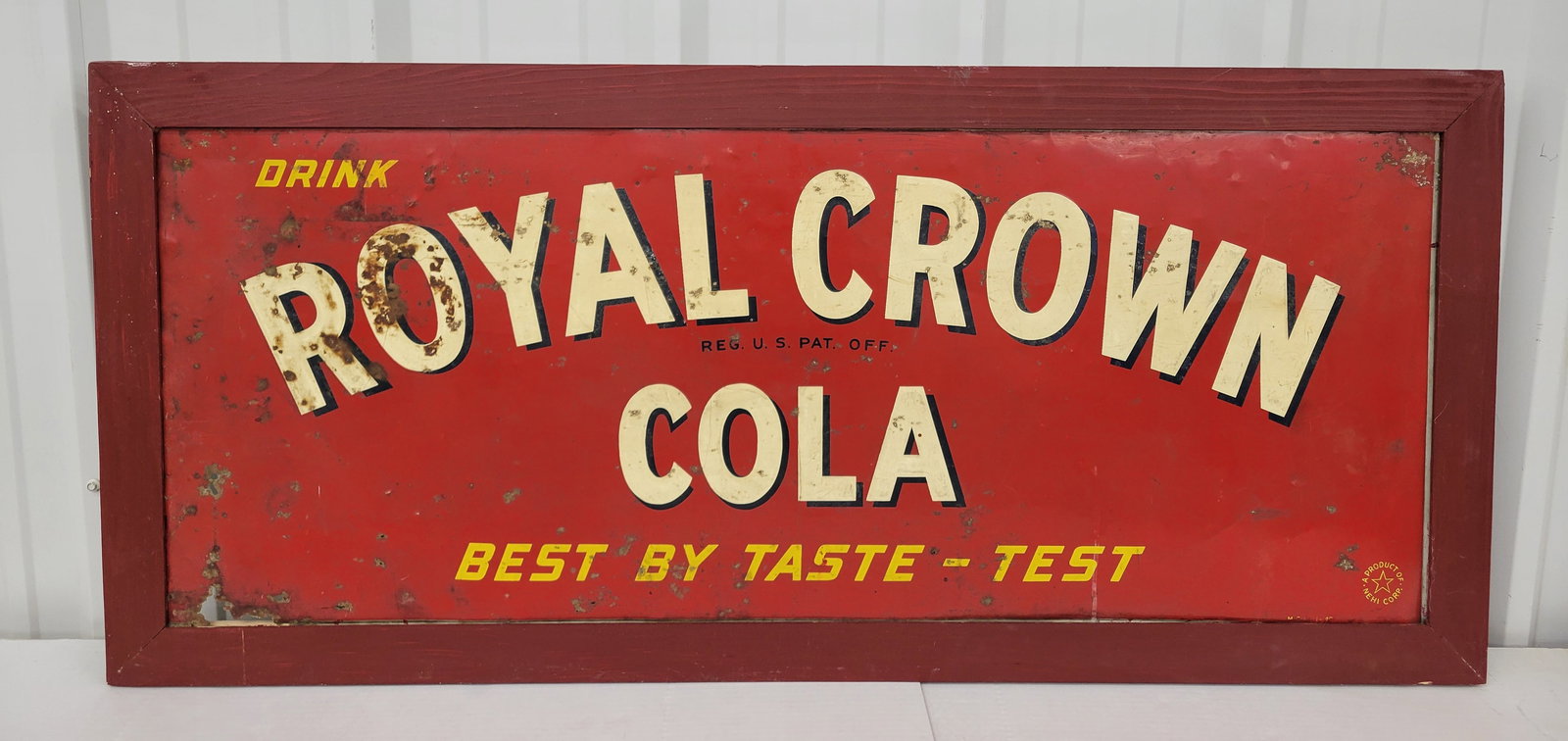 Royal Crown Cola Single Sided Tin Sign In Frame: 54" x 24" SST sign within a wooden frame, shows evidence of wear, including dings, scratches, surface rust, and holes. The painted wooden frame is relatively new and remains in good condition.