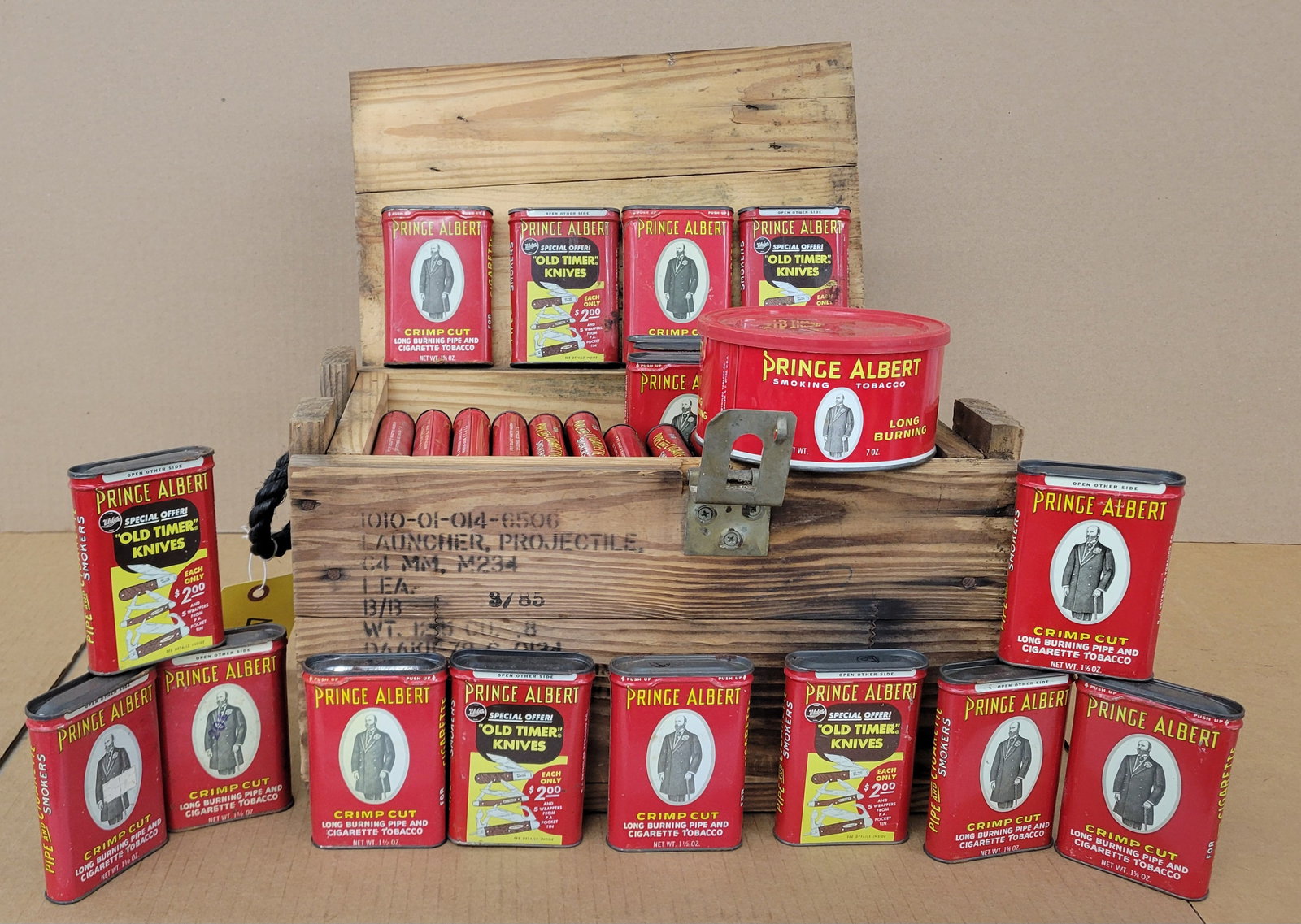 Prince Albert Tobacco Tins and C4 Crate: Lot consists of 63 Prince Albert tobacco tins in varying used conditions and a 15.5" x 10" x 9" wood C4 crate. The crate has rope handles, one hinge, and a latch on top.