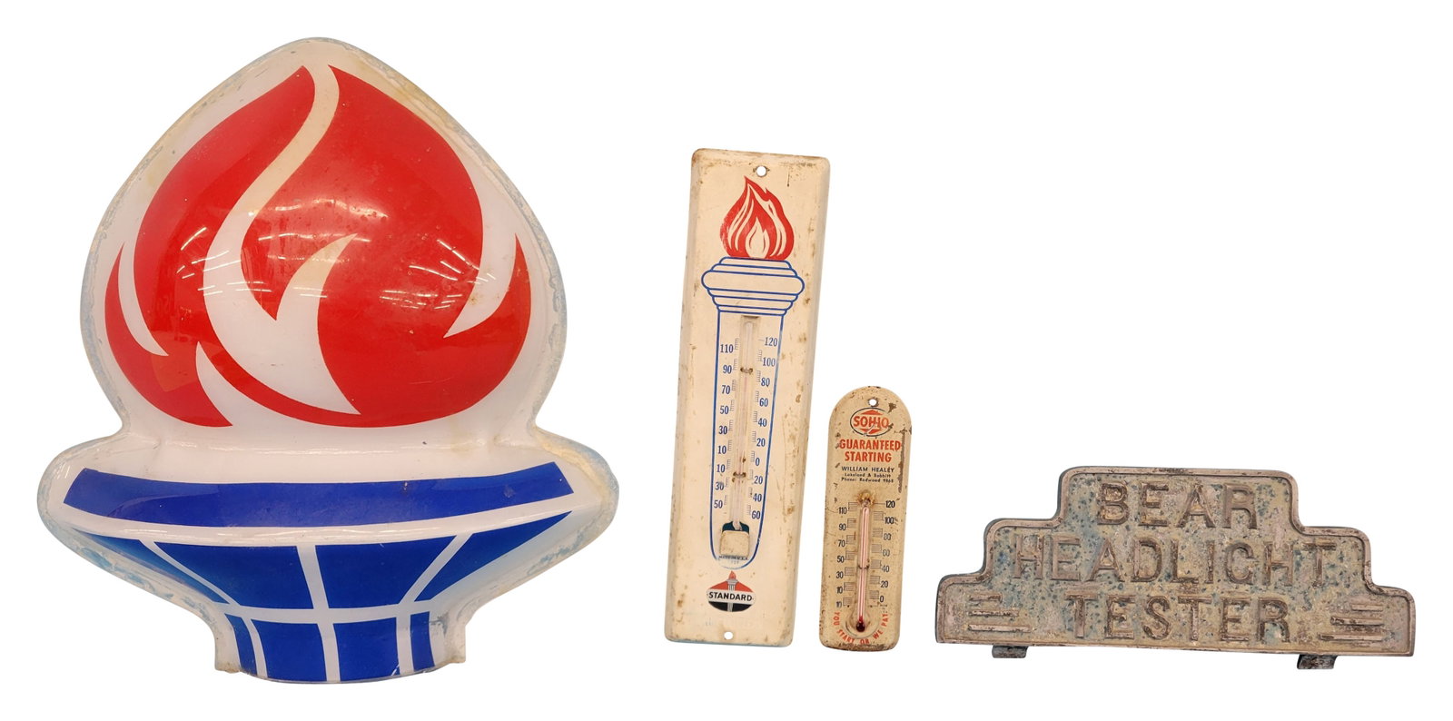 Amoco Gas Torch Flame and misc. lot: This lot features a plastic Amoco Gas torch flame that shows signs of use, including scratches and wear around the edges. Additionally, there is a metal embossed Bear Headlight Tester machine sign top
