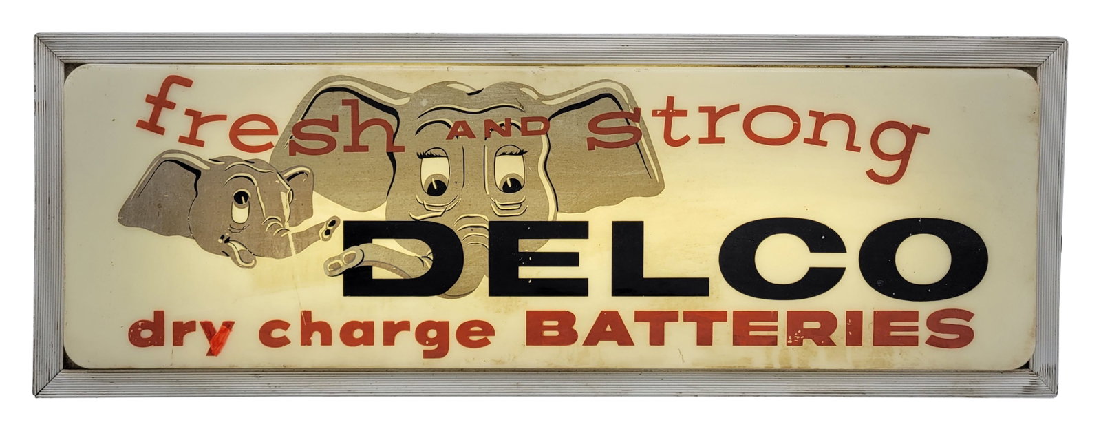Delco Dry Charge Batteries Light Up Advertising Sign: 25.5" x 9" x 3" working illuminated sign features a plastic face and metal housing. There are several light stains and scratches visible on the face although the graphics display well when the sign is