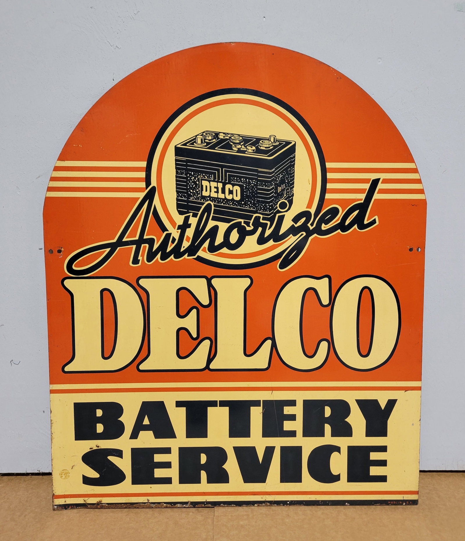 Authorized Delco Battery Service DST Tombstone Sign: 24" x 30" double sided tin sign displays moderate wear throughout each side with light stains and small scuffs and scratches. The bottom edge exhibits flaked paint and surface rust. One of the mount h