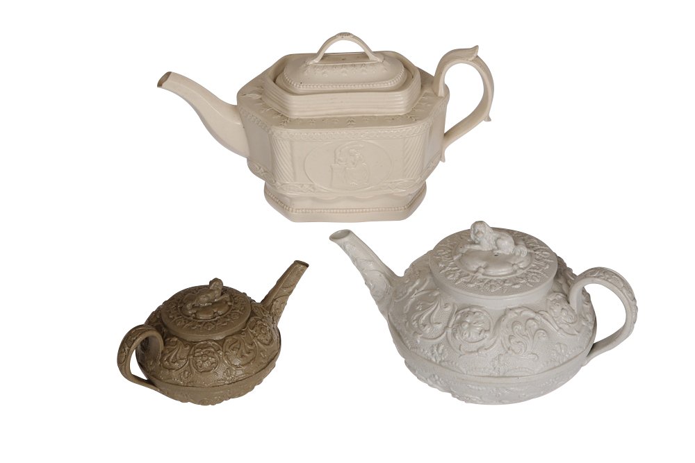A Wedgwood white stoneware teapot: A Wedgwood white stoneware teapot, moulded in relief with scrolling foliage, the cover with King Charles Spaniel knop, impressed WEDGWOOD; together with a smaller Wedgwood buff stoneware teapot, simil