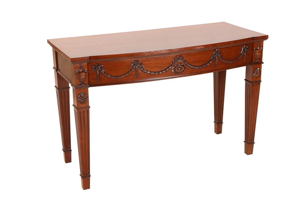 An Adam style mahogany breakfront serving table: An Adam style mahogany breakfront serving table, the rectangular breakfront top above a leaf-carved band over a frieze applied with pendant bellflower swags, raised on square-section fluted tapering l