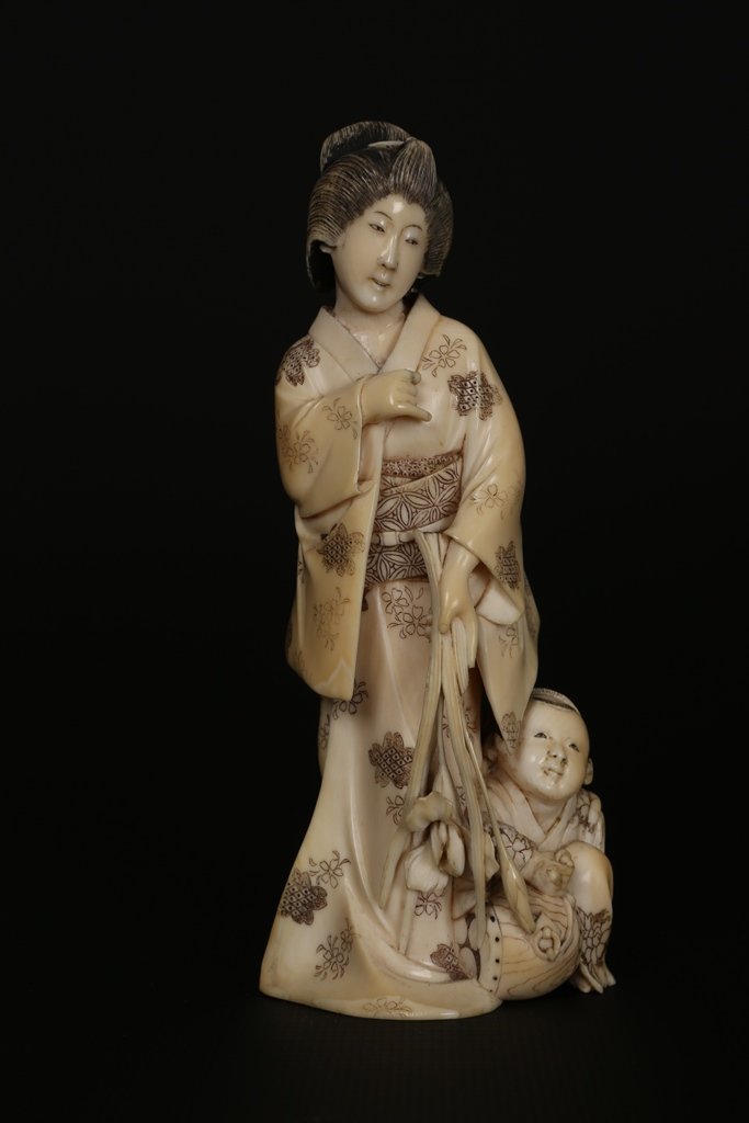 A Japanese ivory Okimono: A Japanese ivory Okimono, Meiji period, modelled as a Geisha in flowing robes with a child at foot, signed to base. 13.5cm