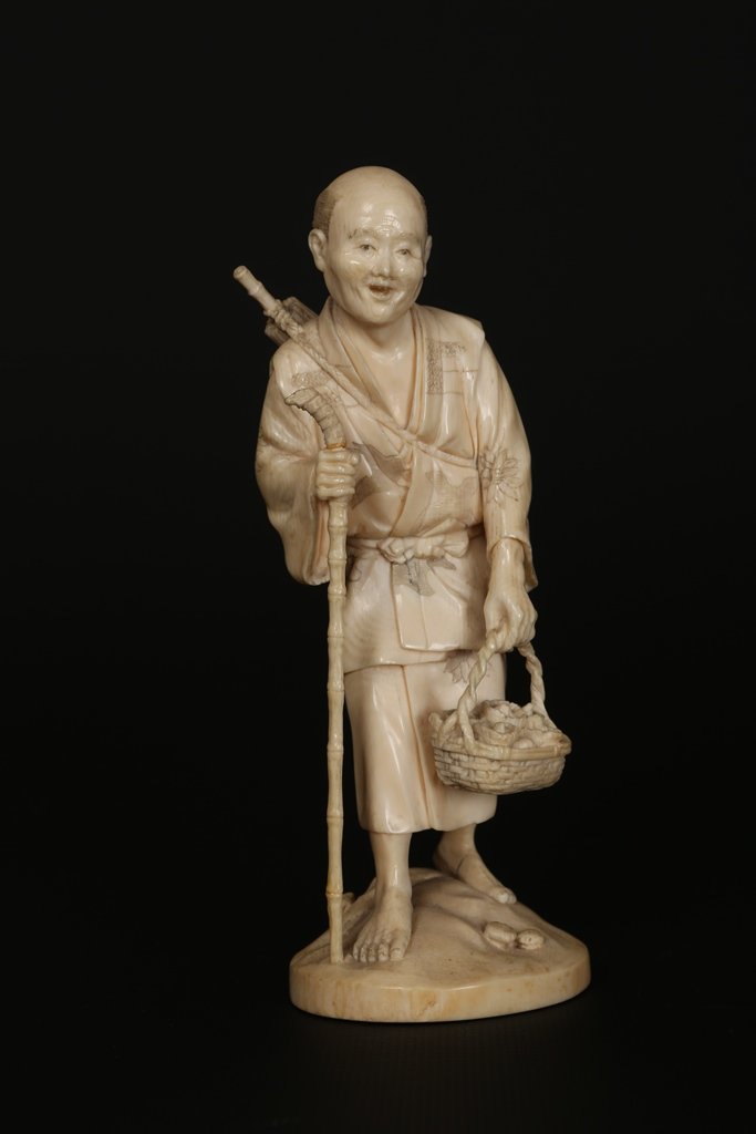 A Japanese ivory Okimono: A Japanese ivory Okimono, Meiji period, modelled as an elder carrying a basket of mushrooms and holding a staff, signed to base. 15cm