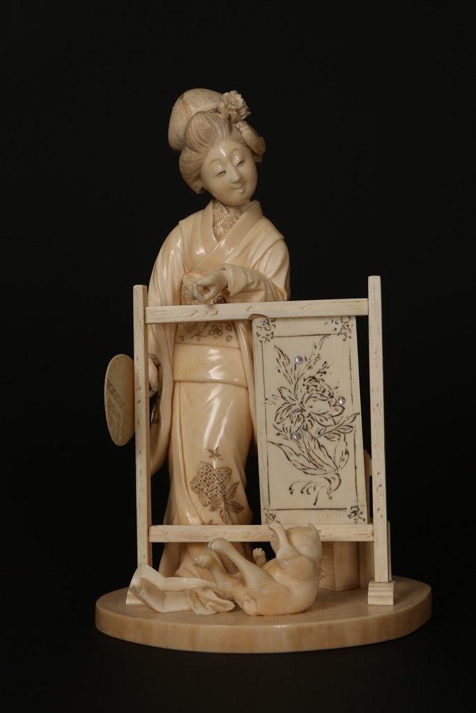 A Japanese ivory Okimono: A Japanese ivory Okimono, Meiji period, modelled as a Geisha with a playful cat beside a screen with sliding panel and four characters verso, signed red plaque inset to base. 20cm