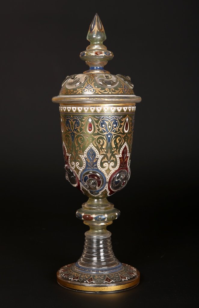 A large Bohemian glass covered goblet: A large Bohemian glass covered goblet, the cover and body moulded with prunts, stained, gilded and engraved with scrolling foliage and alternating red and blue ground panels, raised on a stepped circu