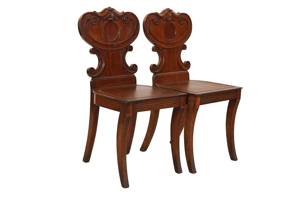 A pair of 19th Century mahogany hall chairs: A pair of 19th Century mahogany hall chairs, with scroll carved backs, raised on reeded sabre legs, (a/f).