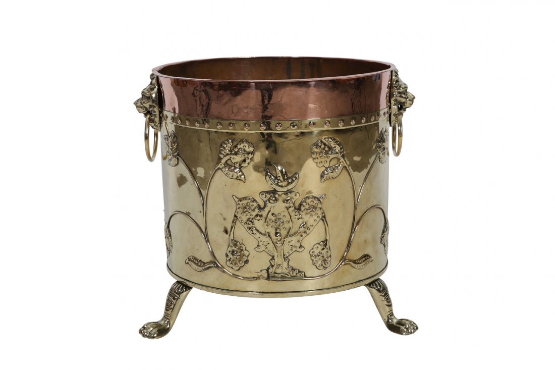 A late Victorian brass and copper log bin: A late Victorian brass and copper log bin, the cylindrical box with lion mask ring handles and repousse with stylised foliage, raised on splayed paw feet. 44.5cm
