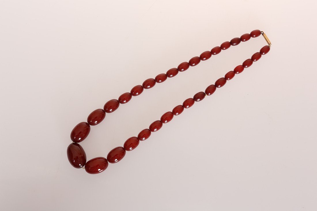 AN AMBER COLOURED BEAD NECKLACE, the thirty three: AN AMBER COLOURED BEAD NECKLACE, the thirty three graduating oval beads strung simply onto an integral tongue barrel clasp. Total length approximately 49cm. Weight 37.7gms.